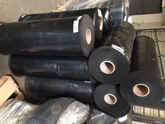 Stacks of black rolled material with white cores, piled in a warehouse or storage area
