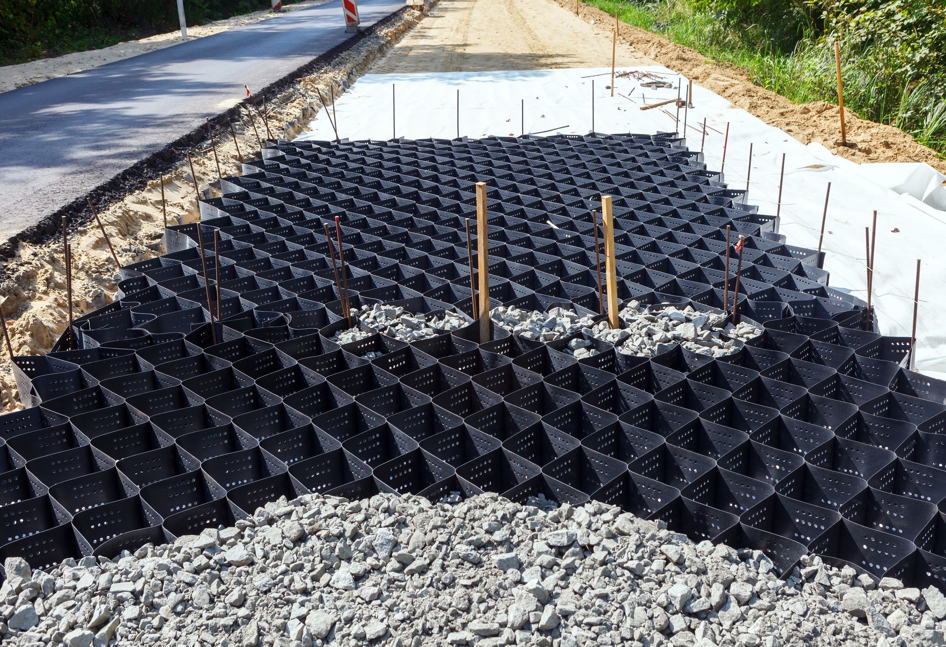 Black plastic ground grid mats on a gravel roadside embankment under construction