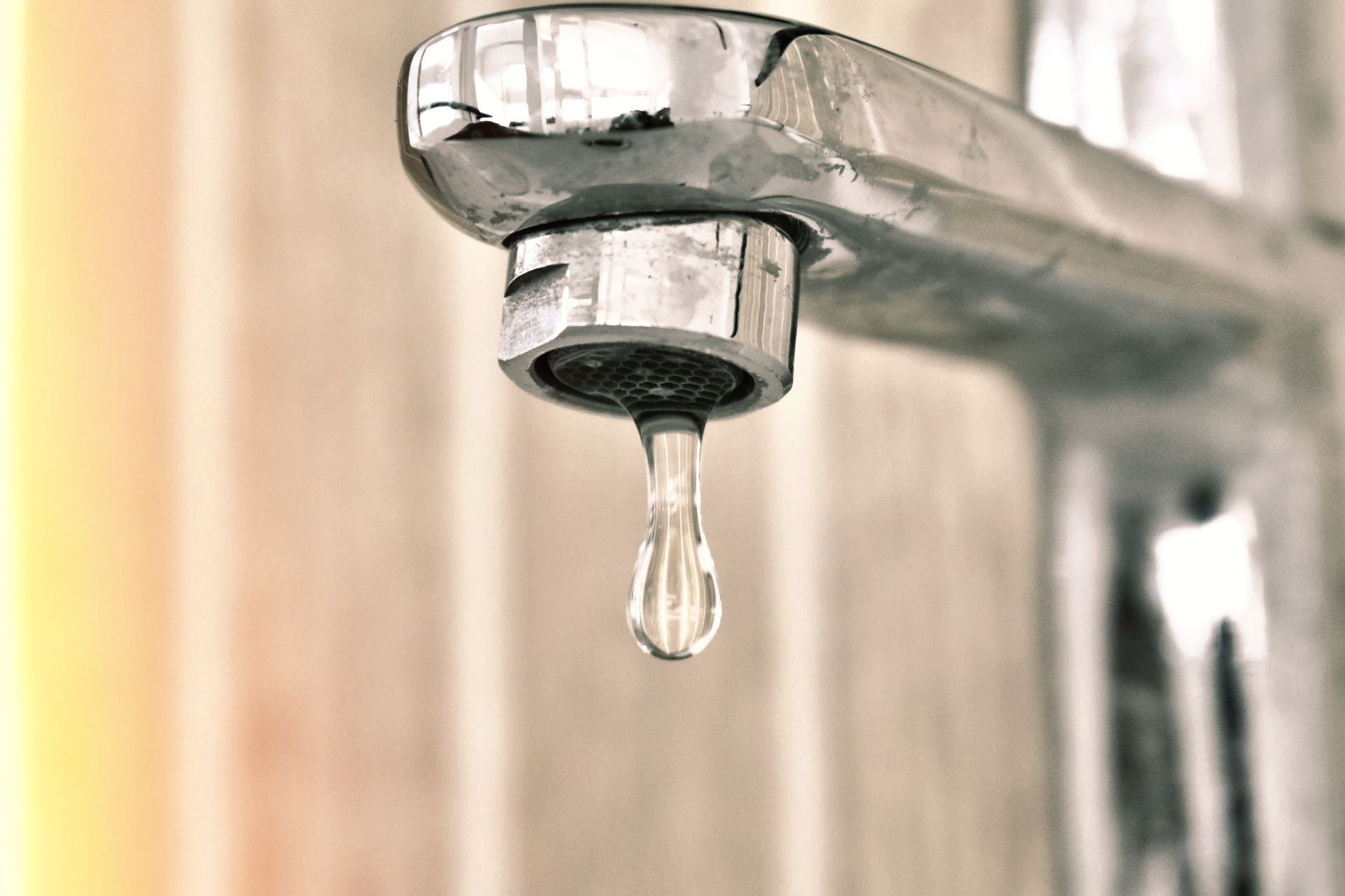 A close up of a faucet with a drop of water coming out of it.