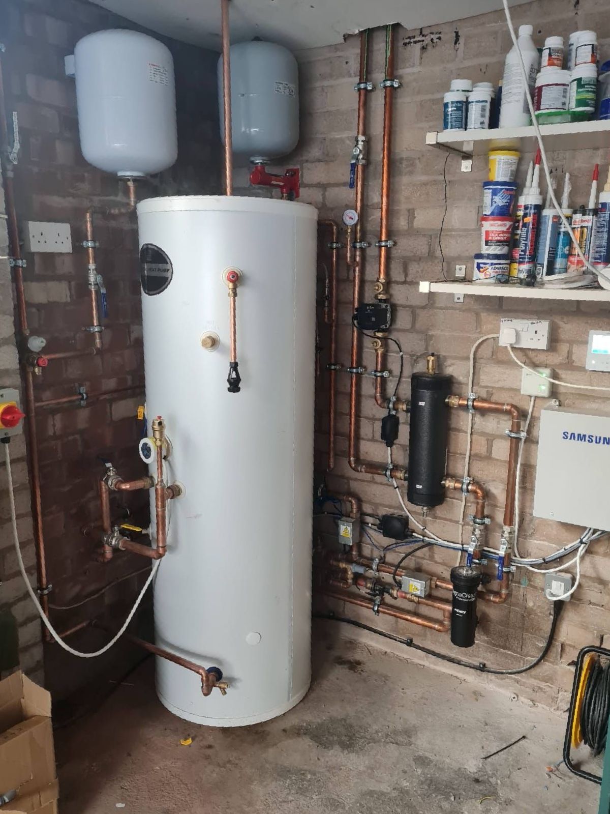 A water boiler heater is sitting in a room next to a brick wall.