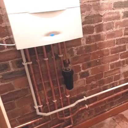 A boiler is sitting on top of a brick wall next to copper pipes.