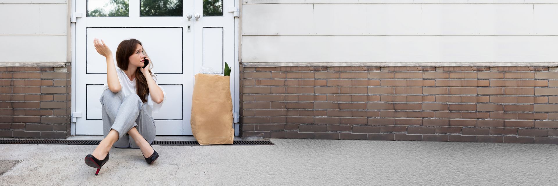 A young woman is waiting in front of a closed door, talking on the phone.