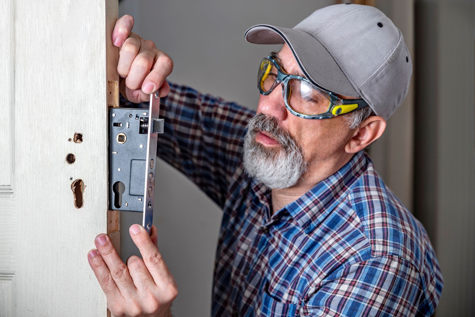 Man installing a door lock, wearing safety glasses and a cap.