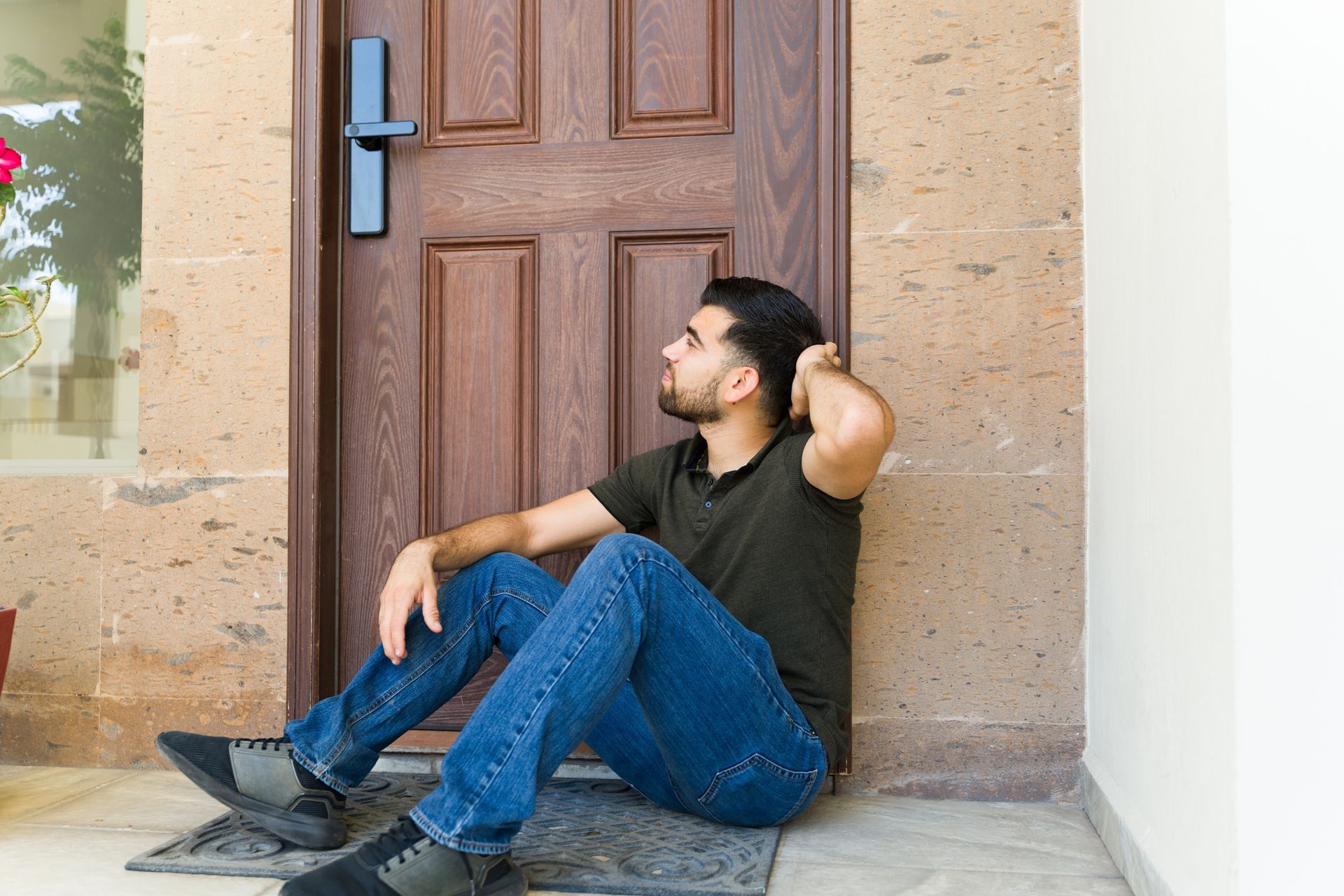 Person sitting on a doorstep in front of a closed wooden door, resting against the doorframe. Person sitting on a doorstep in front of a closed wooden door, resting against the doorframe.
