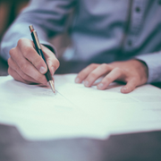 Hands writing on a white sheet of paper with a pen at a desk