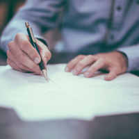 Hands writing on a white sheet of paper with a pen at a desk