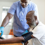 Healthcare worker taking blood pressure from a seated man in a bright room