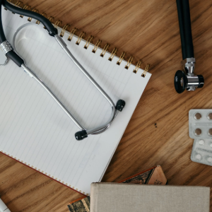 A notebook with a beaded wire bracelet, pliers, beads, and craft supplies on a wooden table