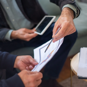 Two people review documents on a couch, one holding a smartphone and the other holding papers.
