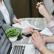 Business meeting around a laptop and documents at a table, with a small potted plant in the center.