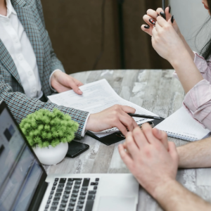 Business meeting around a laptop and documents at a table, with a small potted plant in the center.