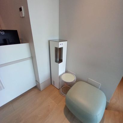 Piccola stanza moderna con un mobile bianco, uno specchio alto, un cesto intrecciato e un pouf verde chiaro su un pavimento in legno.