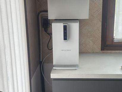 Purificatore d'aria bianco sul bancone della cucina, accanto a una finestra e alle tende.