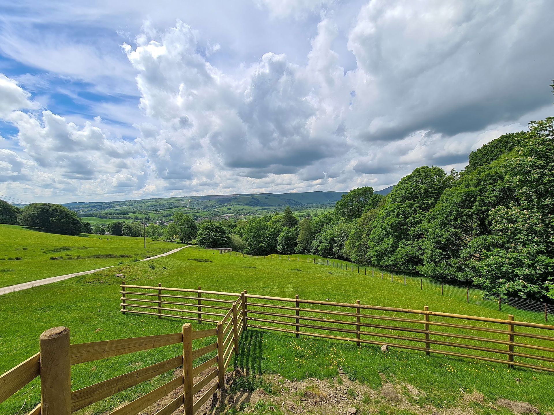 Green countryside hillside with wooden fence under a dramatic cloudy sky