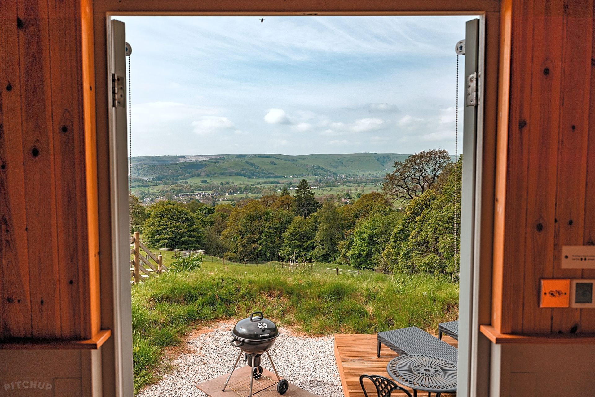 Open doorway to a grassy patio and distant green hills under a cloudy sky