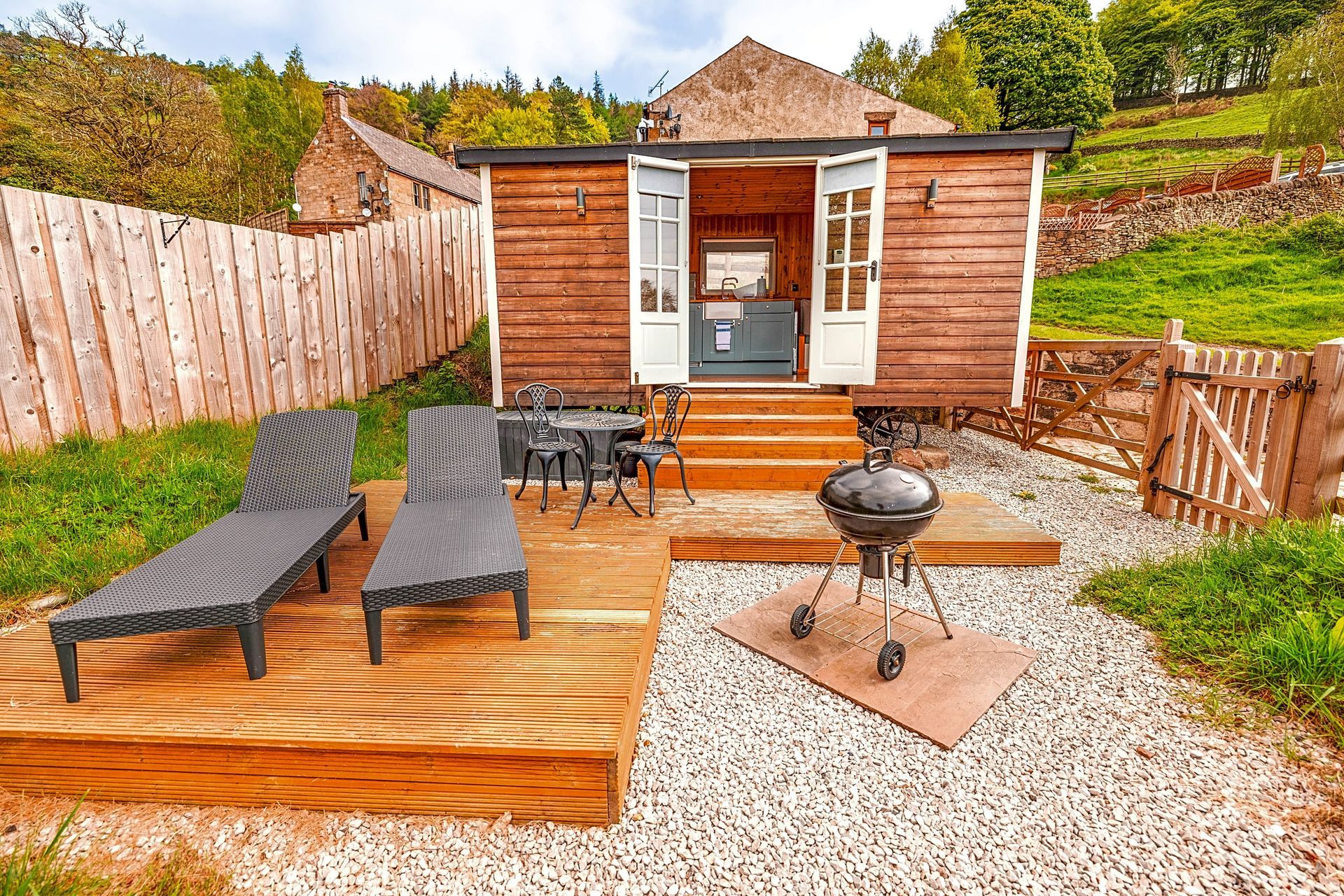 Wooden backyard deck with two lounge chairs, a small grill, and a tiny cabin-style shed.