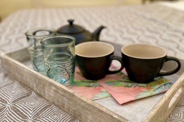 Teapot, two black mugs, and two turquoise glasses on a tray atop a patterned cloth.
