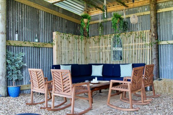 Rustic covered patio with wooden chairs, blue bench cushions, and a small round table