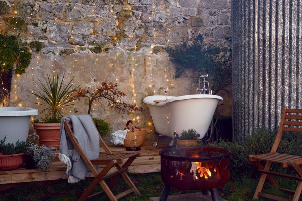 Cozy patio with a lit wood-fired soaking tub, chairs, potted plants, and a stone wall at dusk
