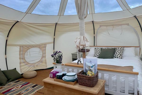 Cozy white tent bedroom with a bed, wooden table, and breakfast tray in a bright glamping setup