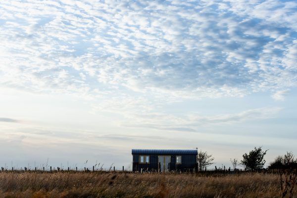 Small blue house in a grassy field beneath a cloudy sky at dawn or dusk