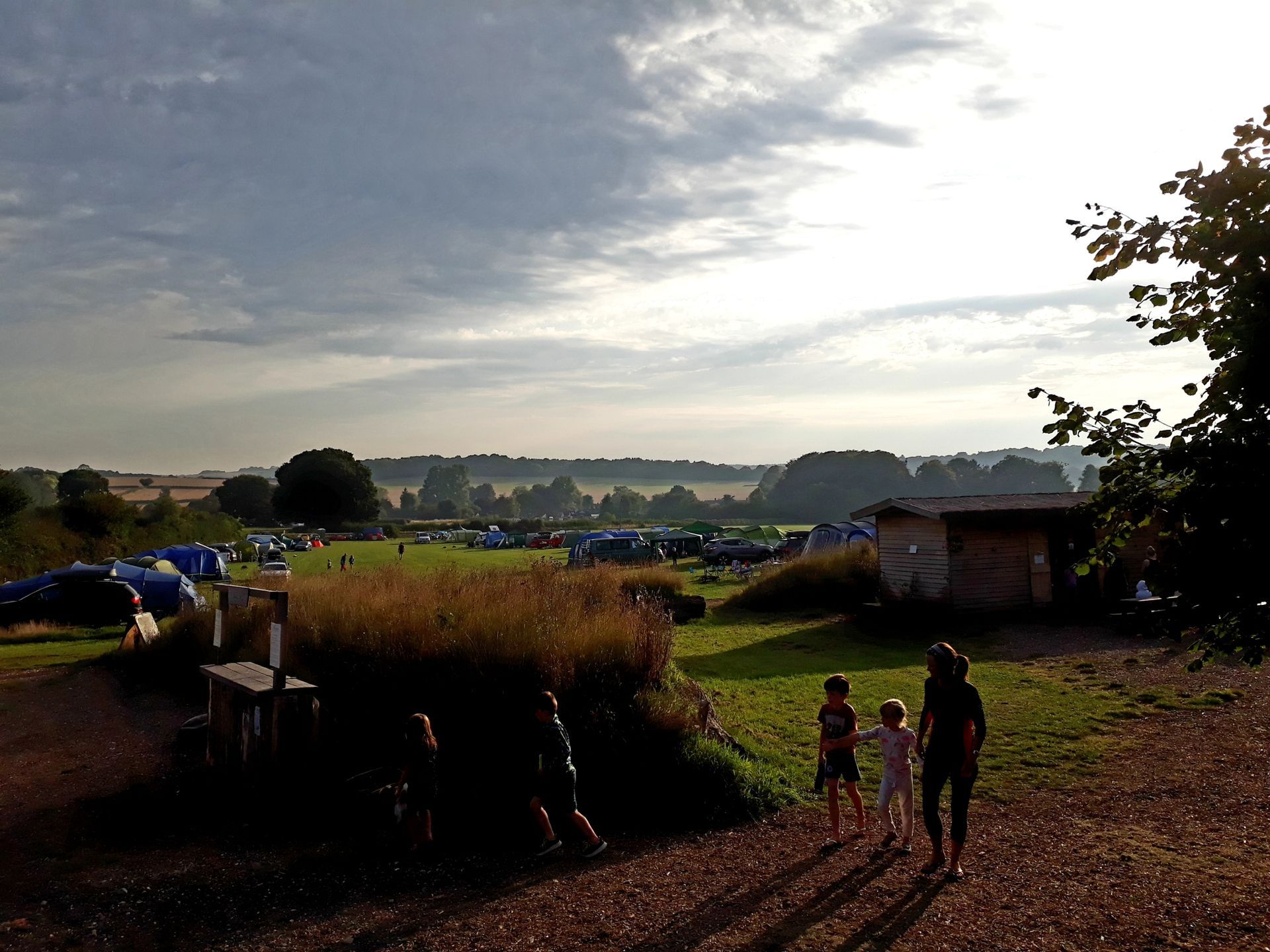 Sunlit rural path beside fields, with three people walking toward a village at dusk.