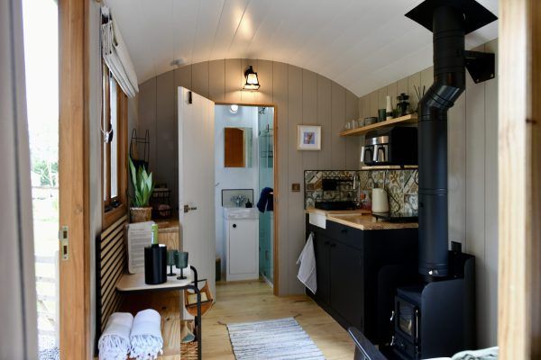 Narrow tiny home kitchen with wood-paneled walls, black stove, white door, and skylight.