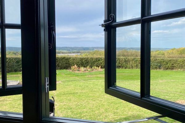 Open window frames a bright green field and cloudy sky beyond a hedge