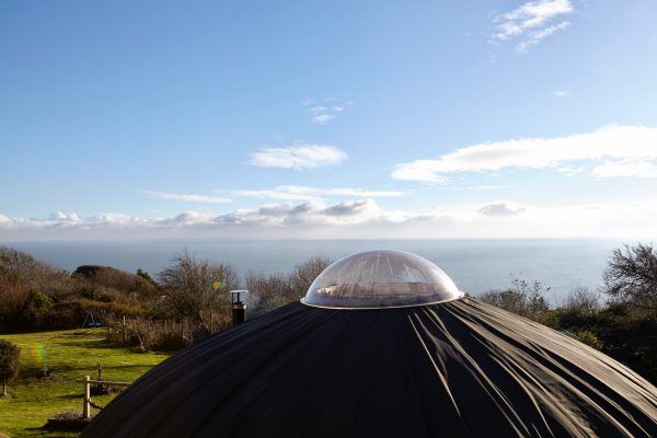 Black dome roof with a clear skylight overlooking a sunny coastal landscape and blue sky