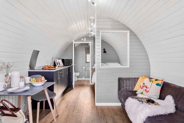 Bright attic dining nook with a desk, gray chair, sofa, and large round window ниша