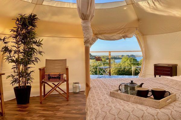 Luxury tent bedroom with canopy bed, wooden chairs, and a view of the sea through the open entrance