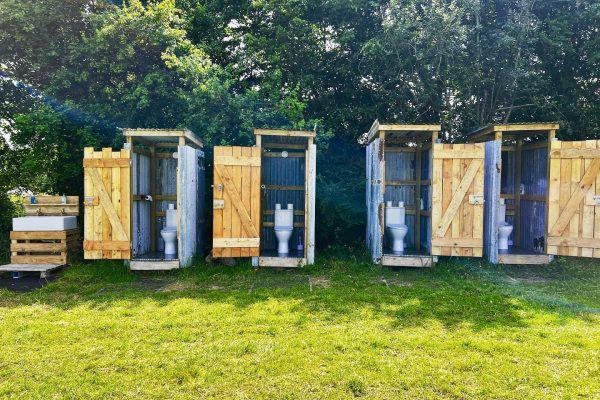 Outdoor row of three wooden portable toilets on a grassy lawn with trees behind them