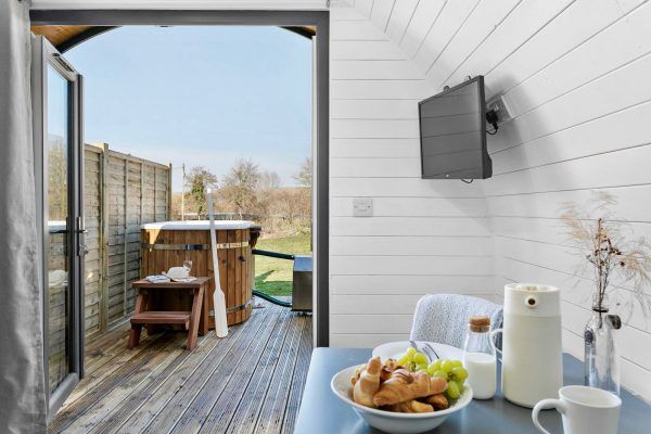 Patio with open doors, wooden deck, and breakfast tray with fruit, roll, and coffee on a table