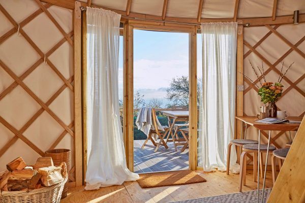 Cozy yurt interior with open doors to a lake-view deck and white curtains