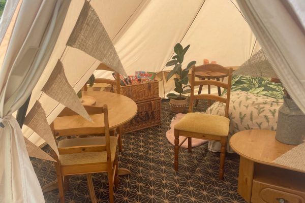 Cozy tented café nook with wooden tables and chairs, patterned rug, and warm draped fabric walls