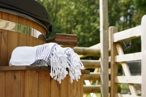 White towel draped over a wooden hot tub beside a white fence outdoors
