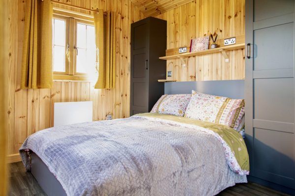 Cozy wood-paneled bedroom with a bed, gray wardrobe, window, and shelf decor