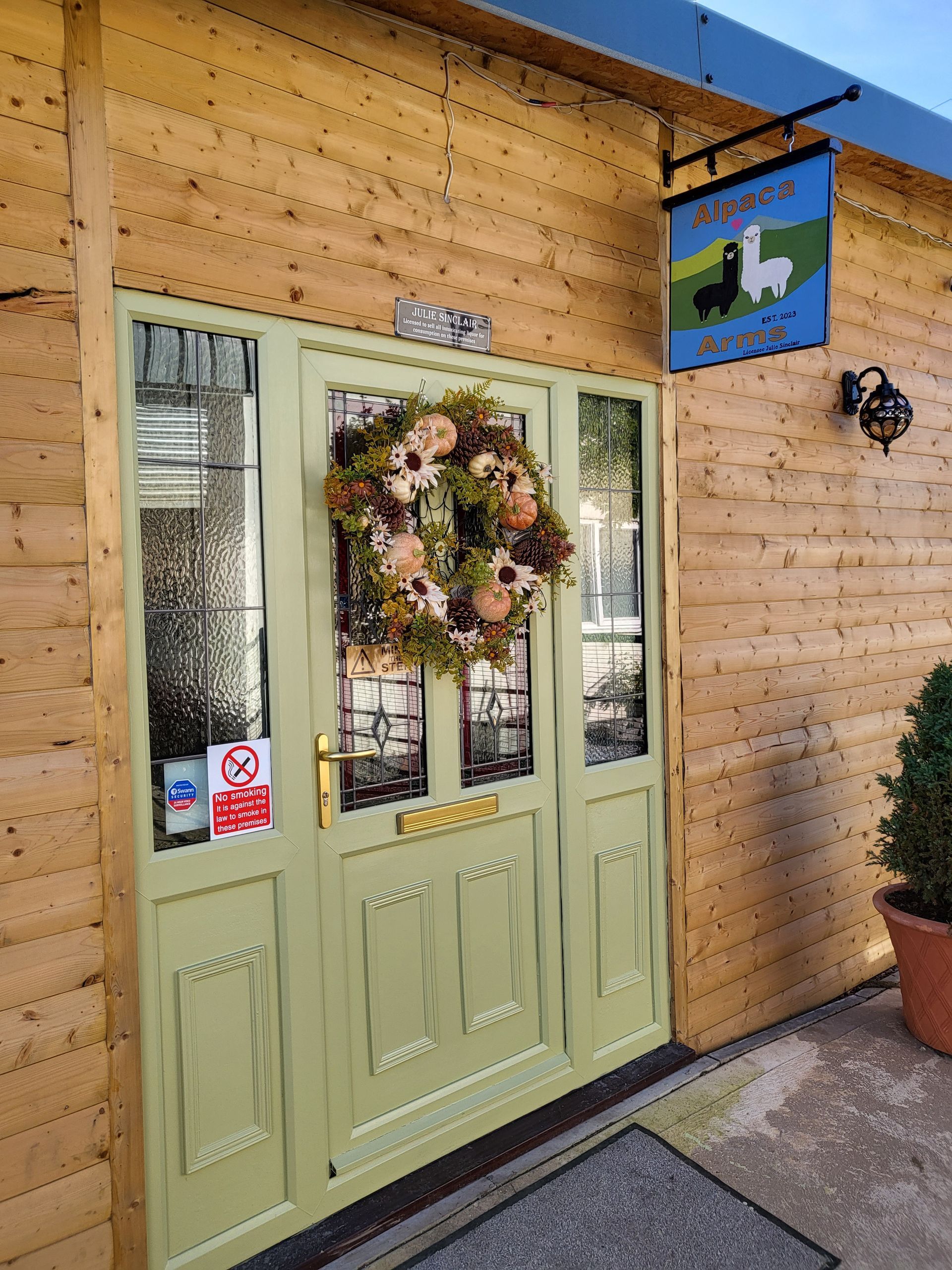 Green double doors with a floral wreath on a wood-paneled storefront entrance