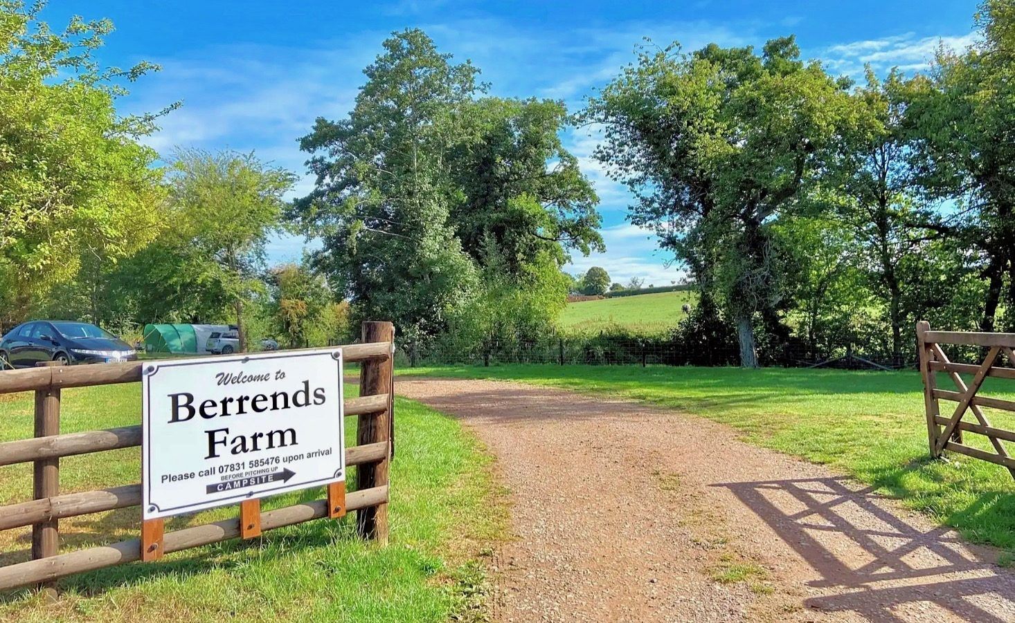 Berends Farm sign at a gravel entrance, with green trees, blue sky, and fields in the background