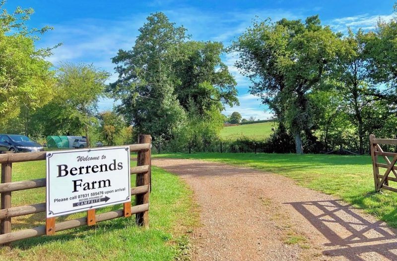 Berrends Farm entrance with wooden gate, gravel drive, and green trees under a blue sky