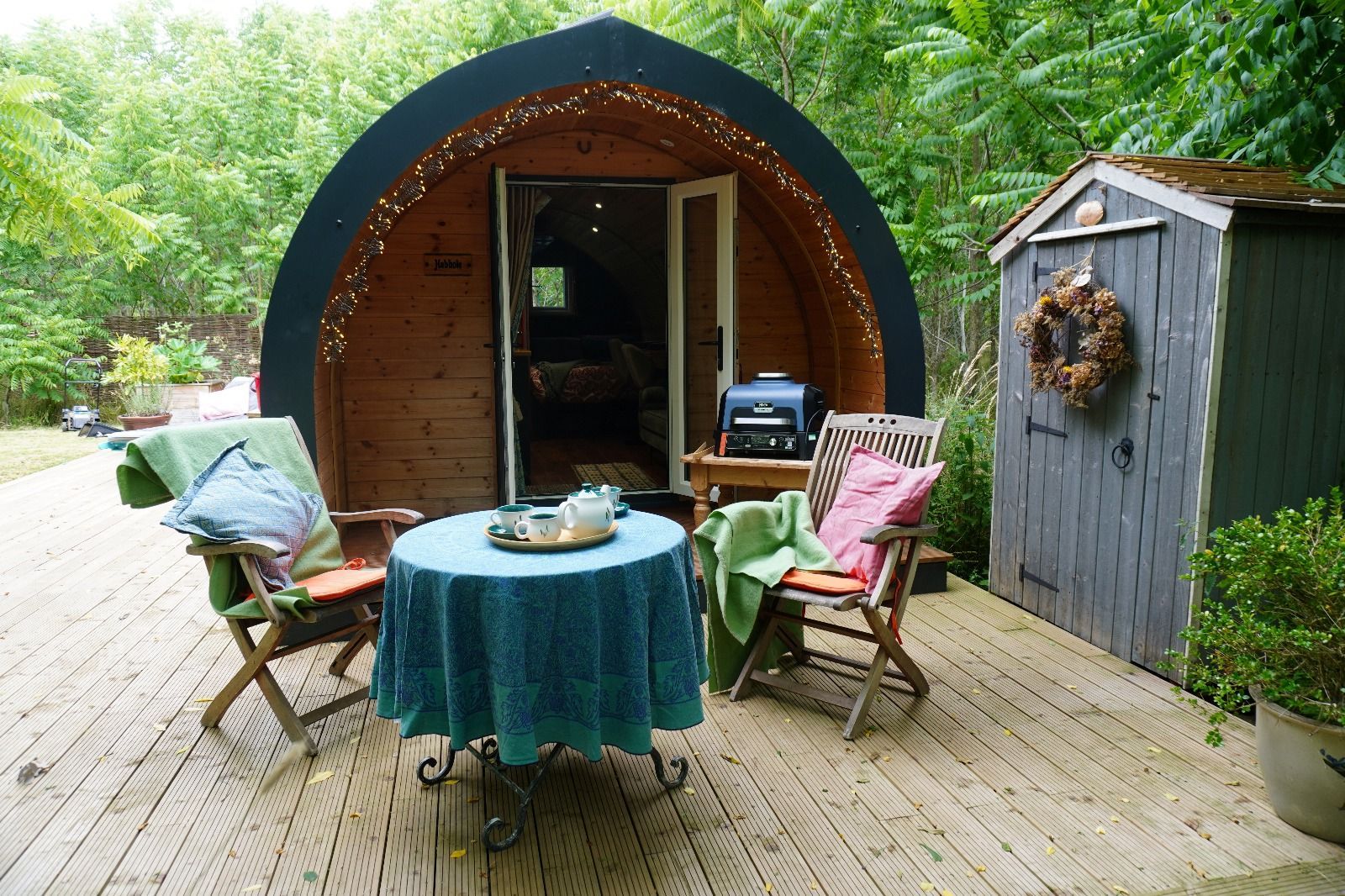 Outdoor patio with two lounge chairs, round table, and a small wooden cabin beside a shed