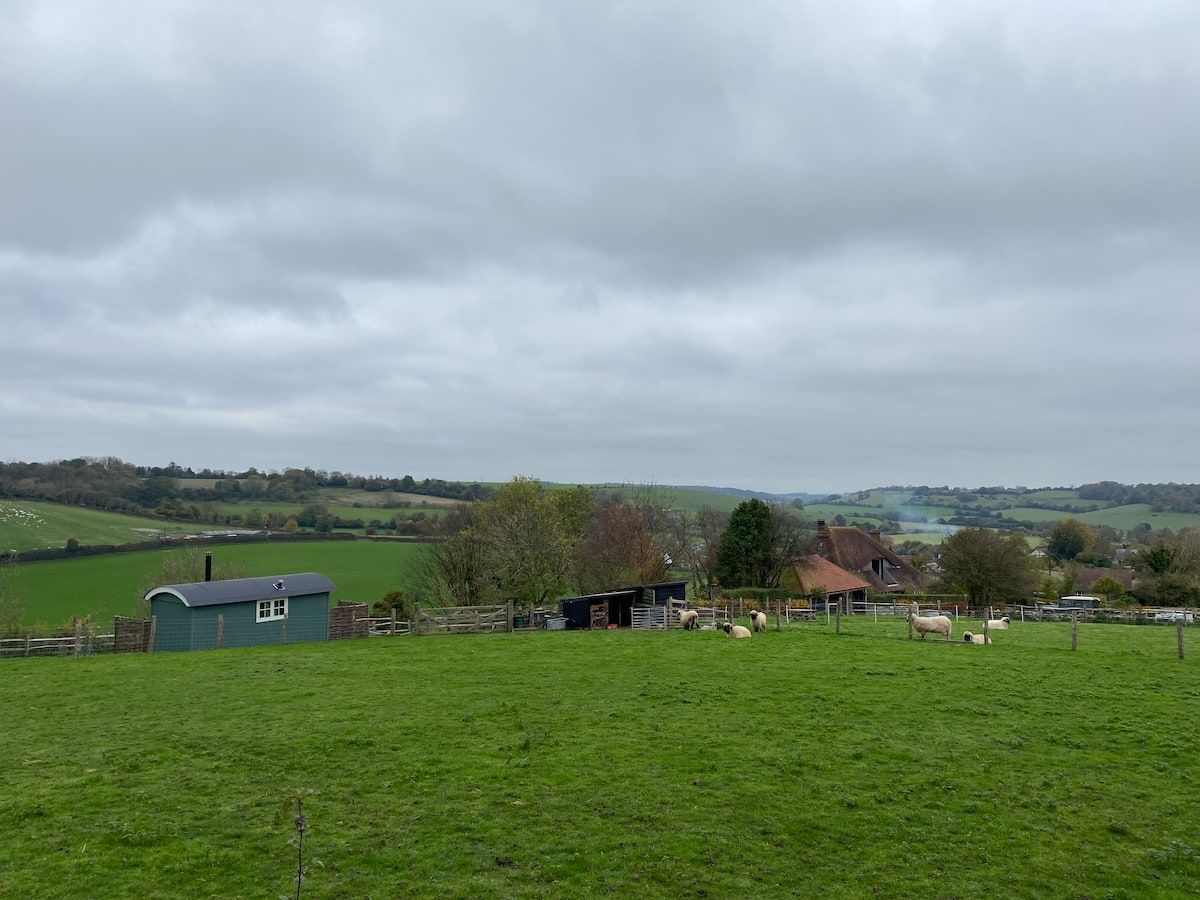 Cloudy rural landscape with green pasture, distant farm buildings, and rolling hills.