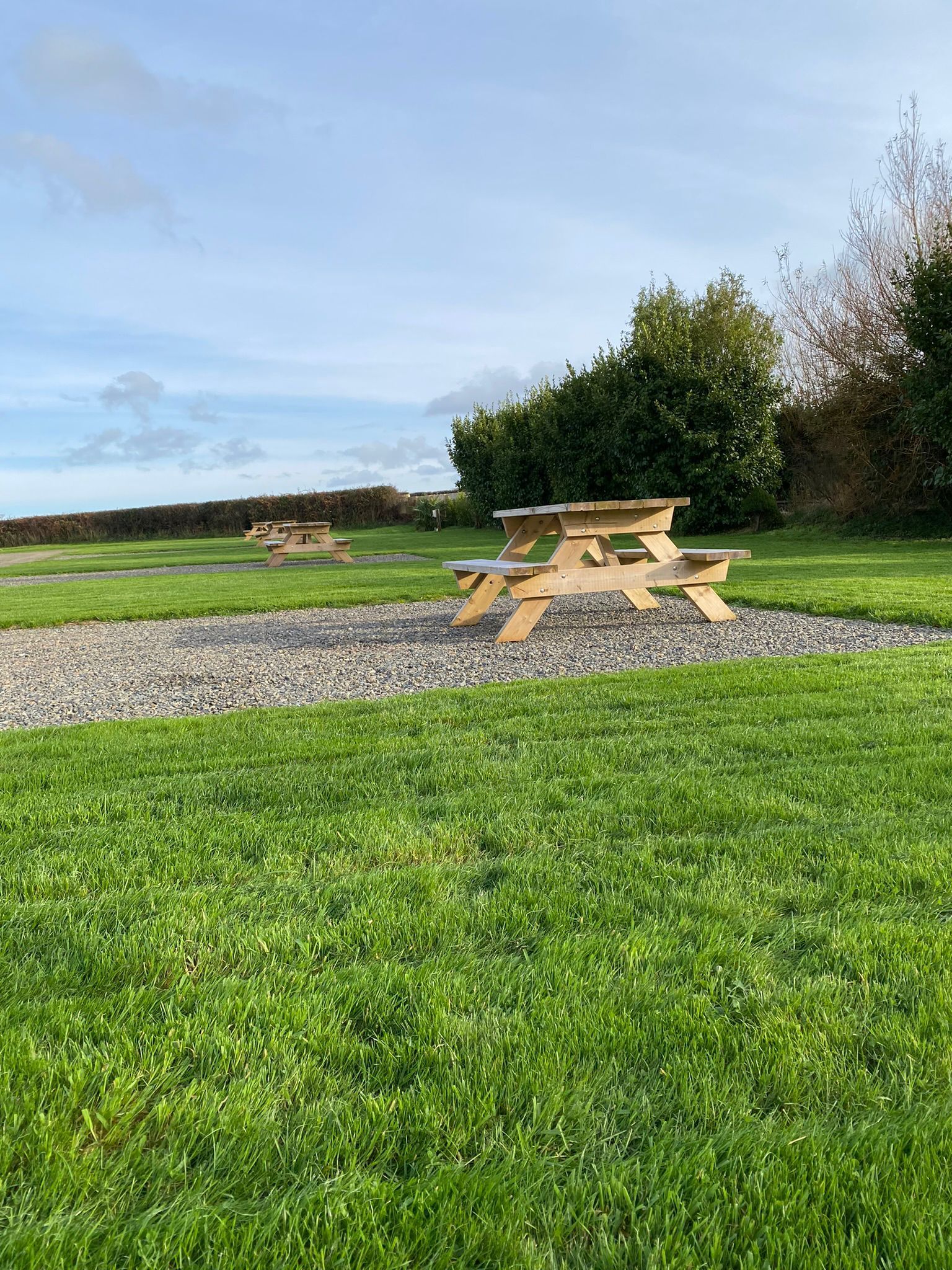 Wooden picnic table on a gravel patch in a grassy field under a blue sky