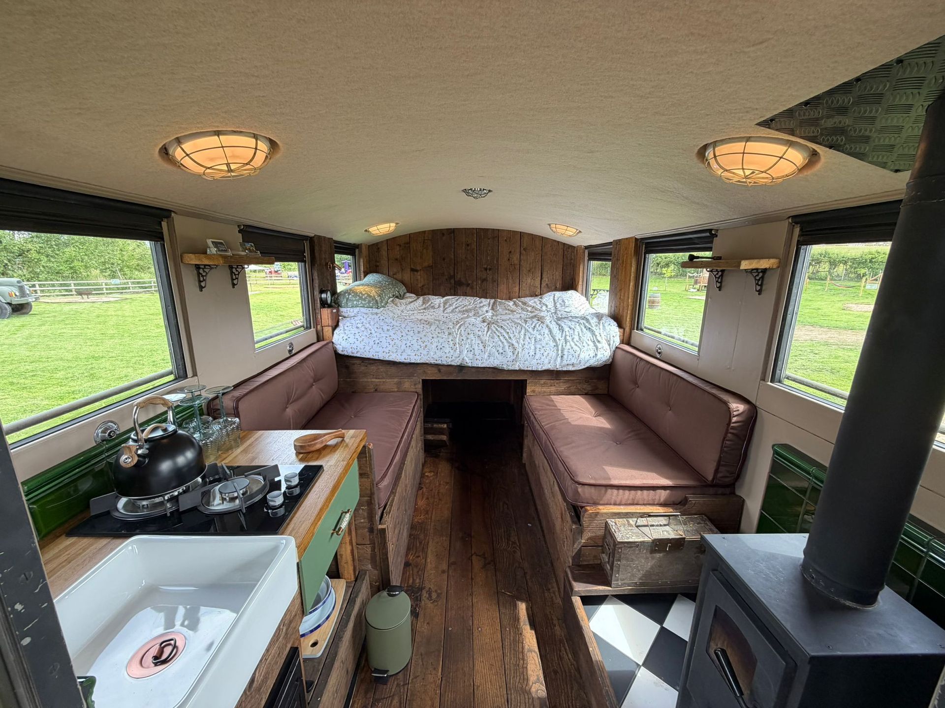 Small RV interior with bunk bed, bench seating, kitchenette, and wood stove.