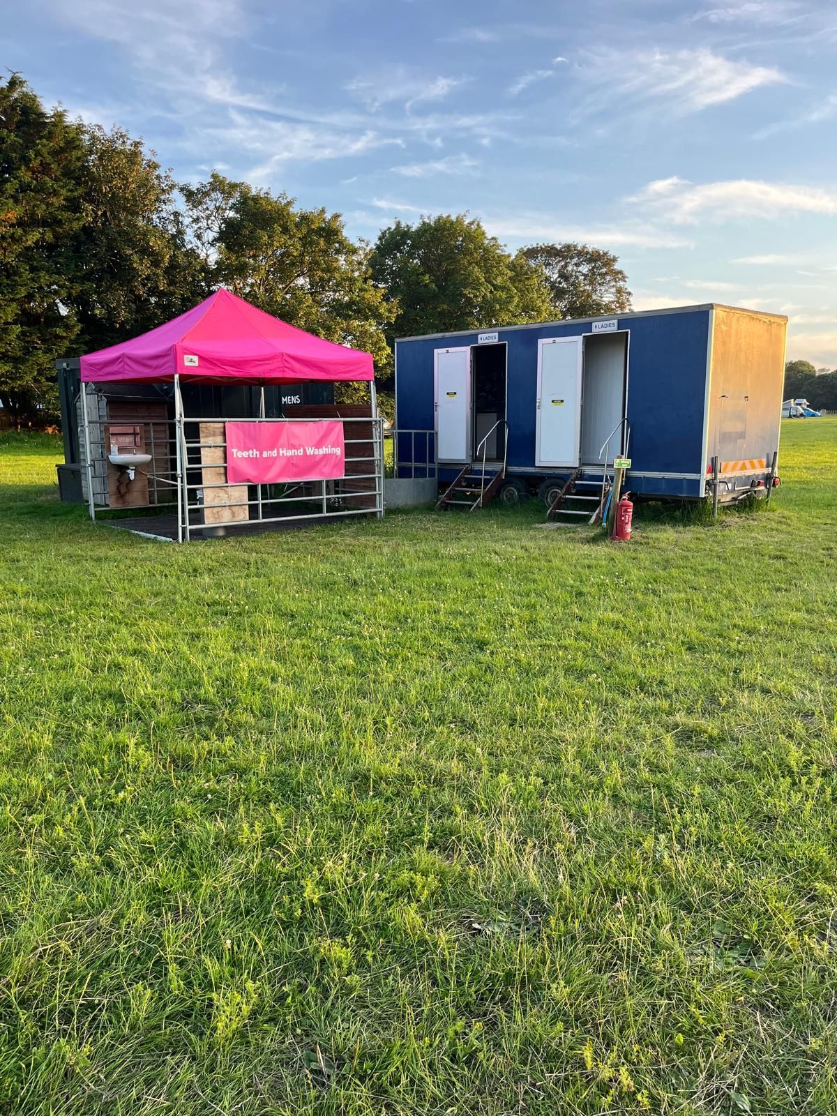 Pink canopy and blue trailer setup on a grassy field at sunset