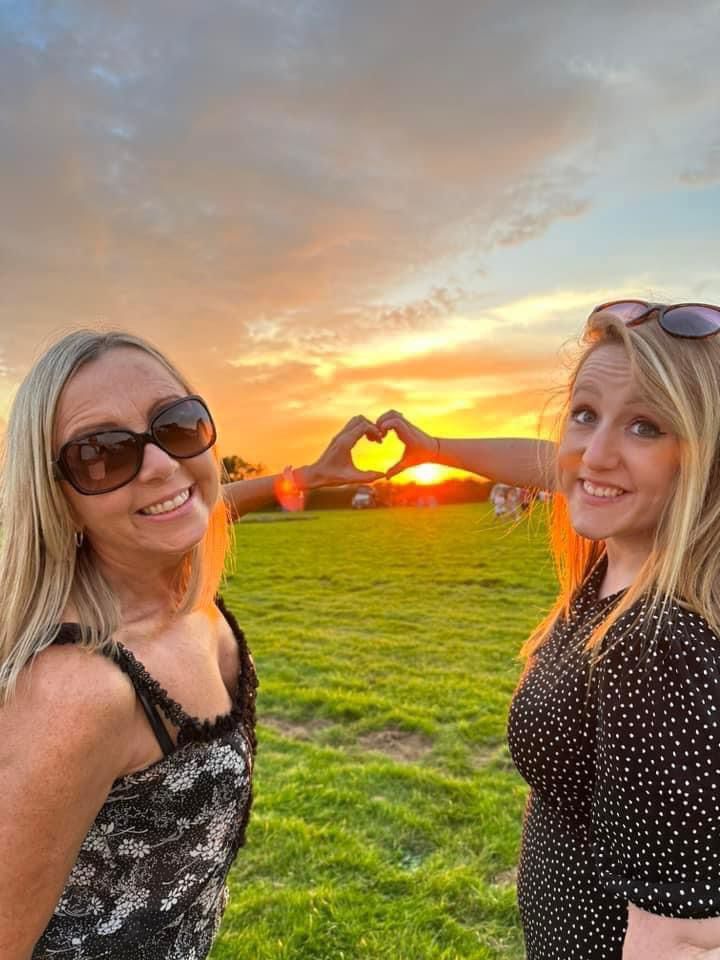 Two women smiling at sunset in a grassy field with a glowing heart shape in the background