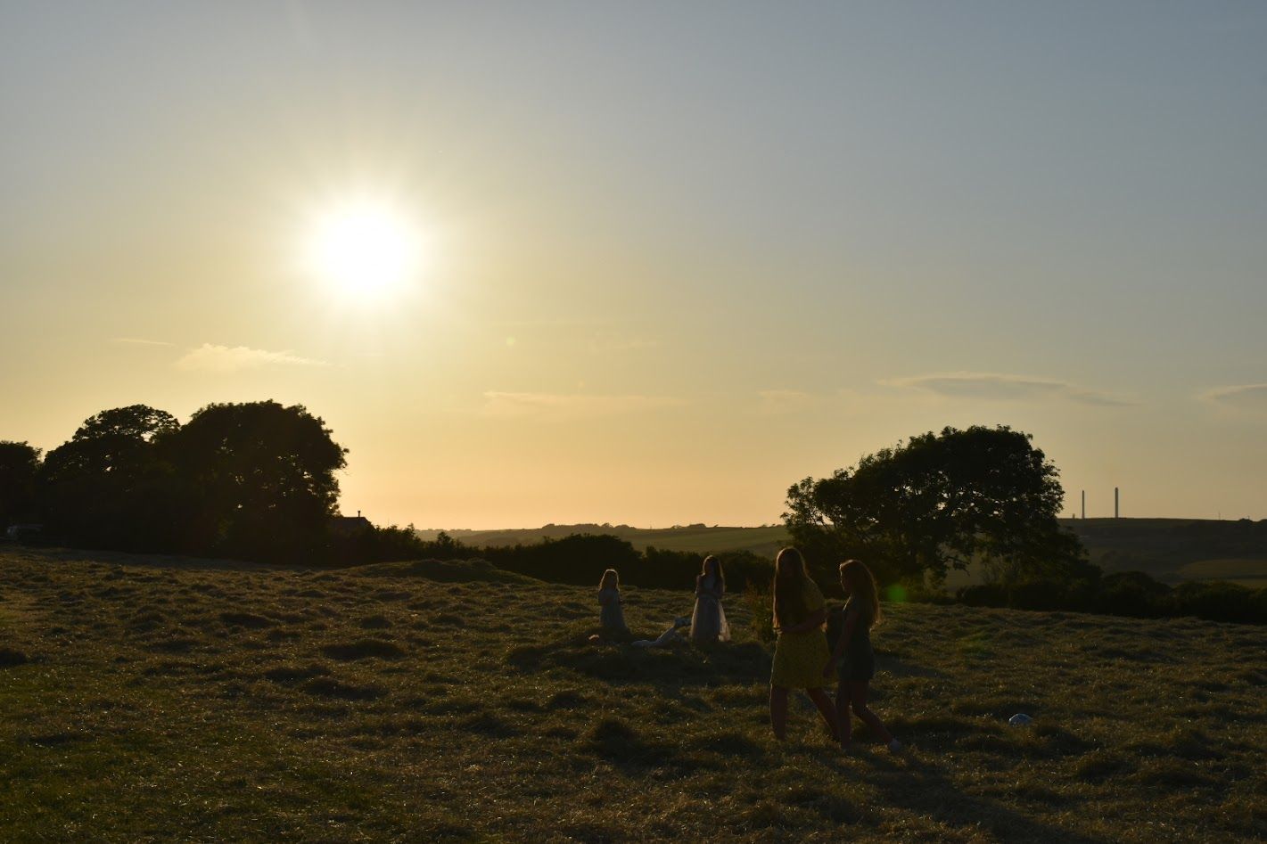 Sunset over a grassy field with silhouetted trees and people in the distance