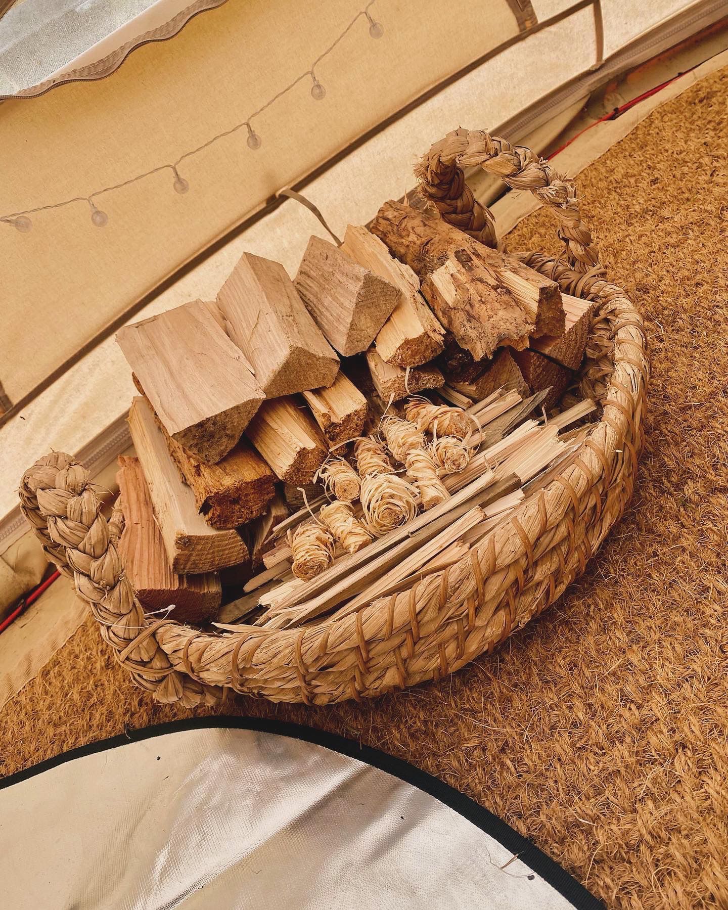 Basket of chopped firewood on a carpeted floor near a stove or fireplace.