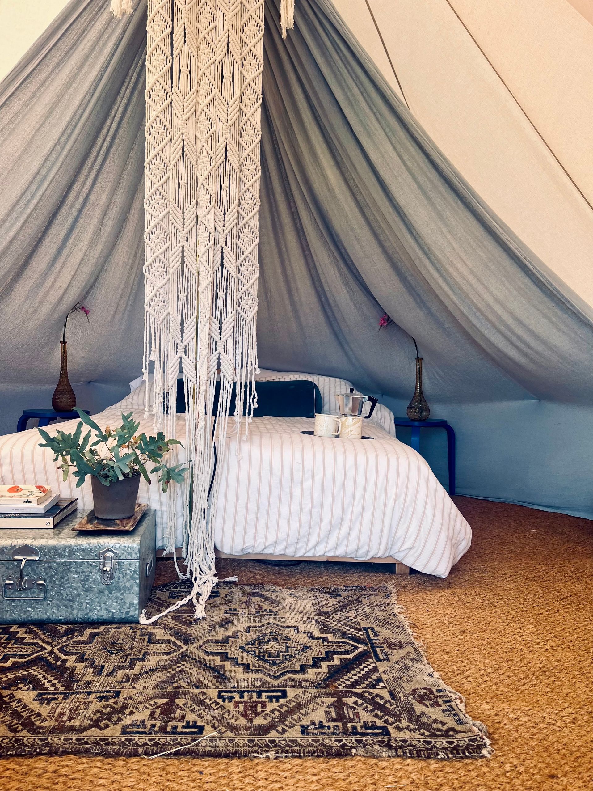 Cozy tent bedroom with white bed, blue drapes, patterned rug, and boho decor