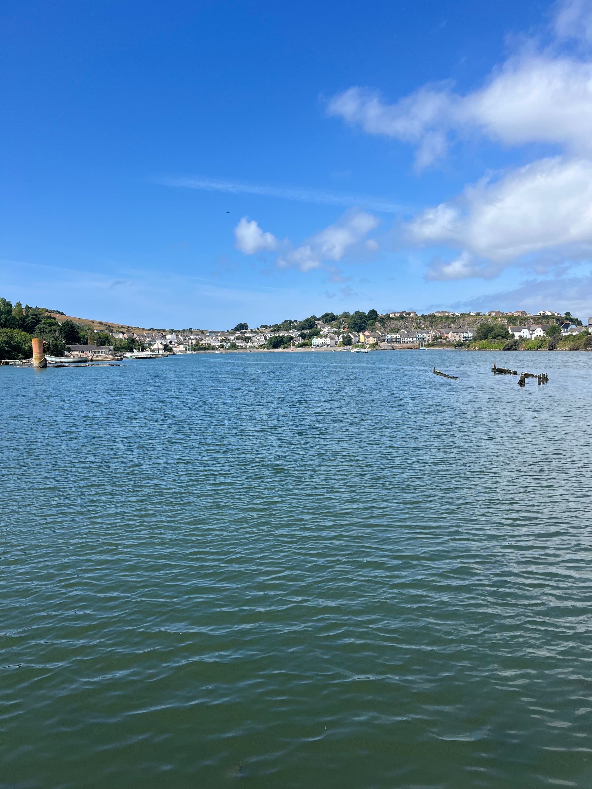Calm blue bay with rippling water, a small sailboat, and a coastal town under a bright sky
